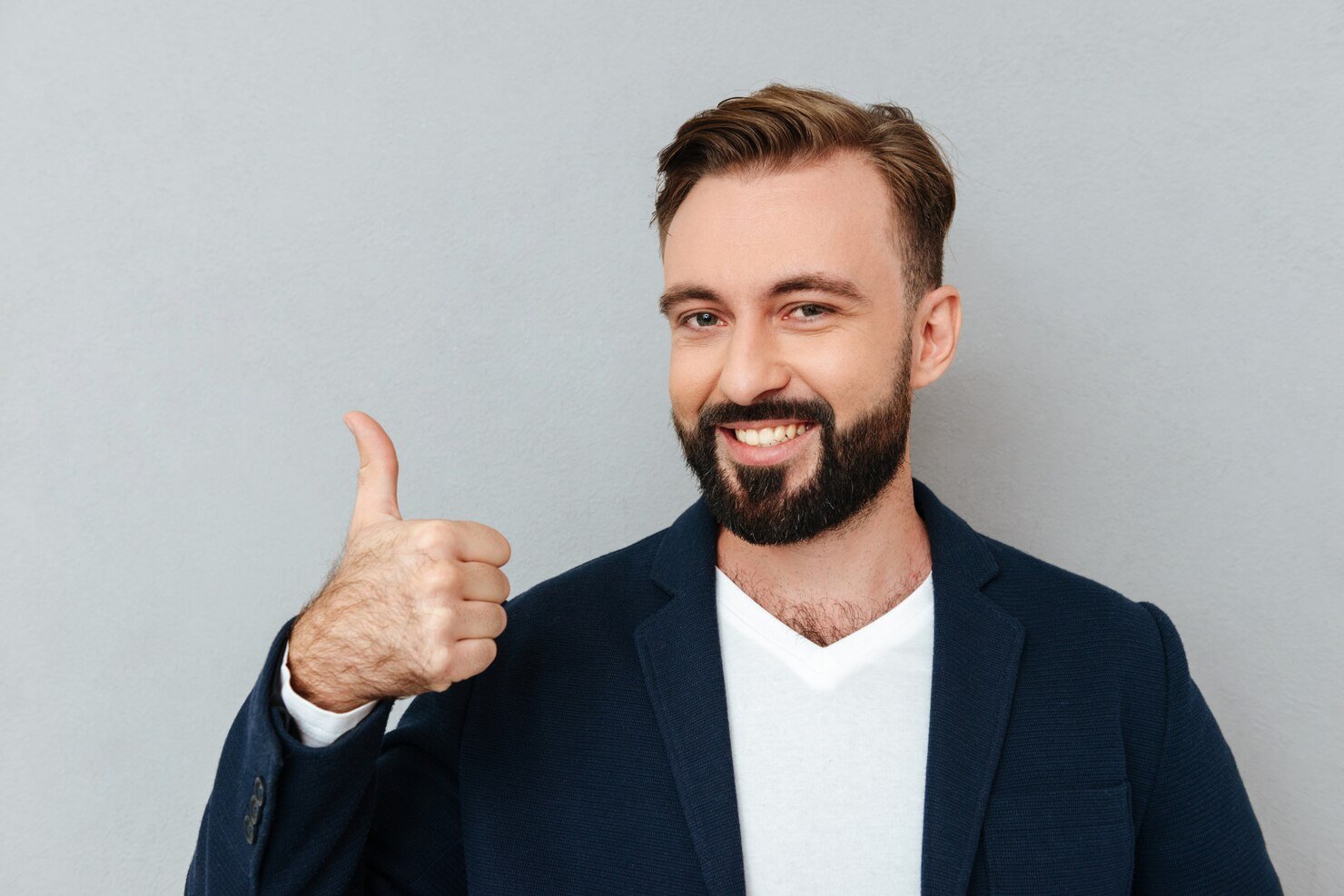 cheerful-bearded-man-busines-clothes-showing-thumb-up-looking-camera-gray_171337-11351